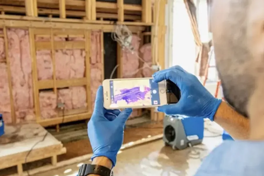 Technician reading a thermal camera against open wall framing during a dry-out