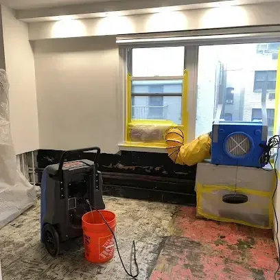 A dehumidifier and an air mover running in a room where the flooring was pulled up to dry the subfloor