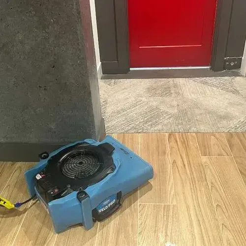 An air mover aimed across a wood-look tile floor beside an open doorway while the room dries out
