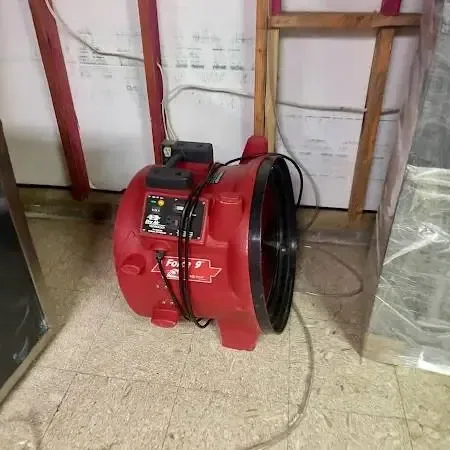 A red air mover beside a lower wall opened up for drying, with plastic sheeting hung around the work area