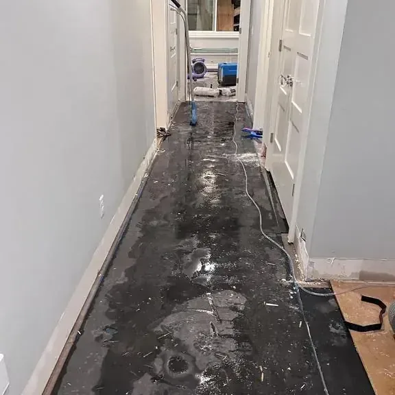 Standing water spread along a dark hallway floor inside a flooded home